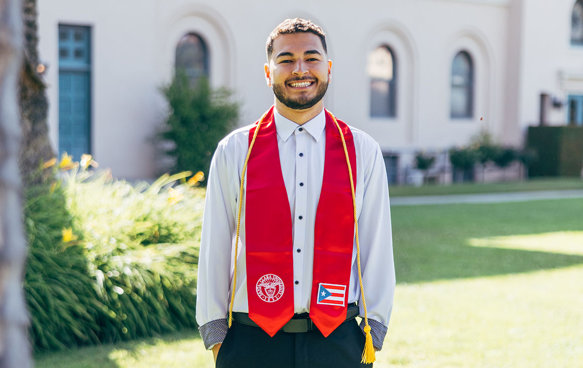 Roberto Mercado poses in graduation attire on the Santa Clara University campus.